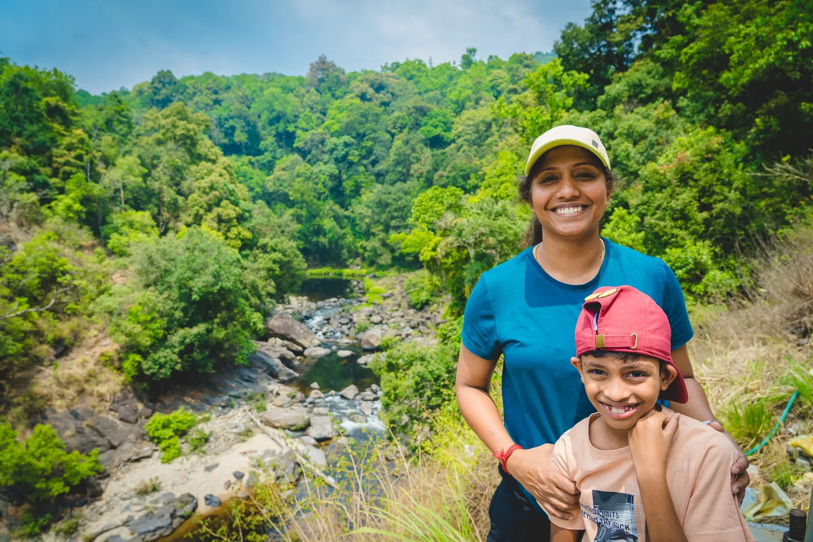 A traveller and child smiling at a viewpoint above a boulder-strewn river valley