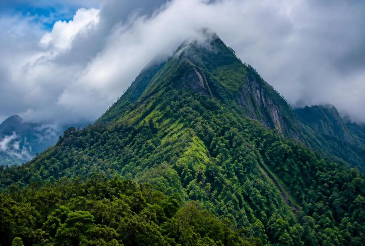 Steep forested peak with clouds moving across the summit